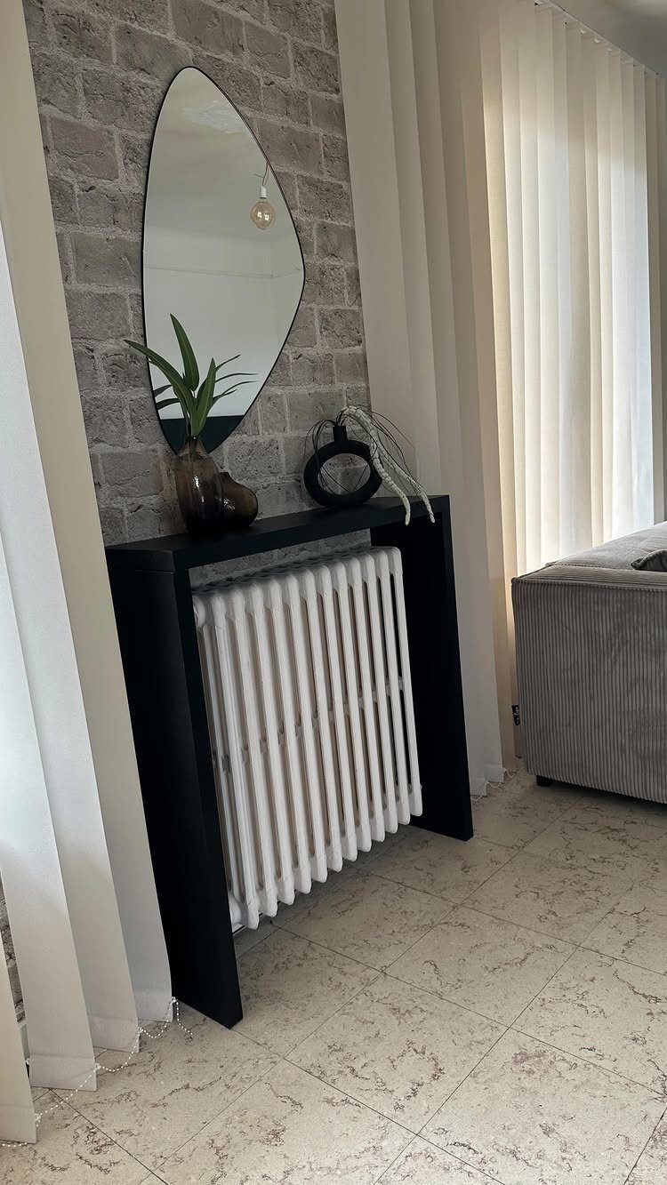 15 Apartment Decor Inspiration Ideas for Small Living Spaces 14 Black radiator cover against a grey brick wall with a mirror and plant.