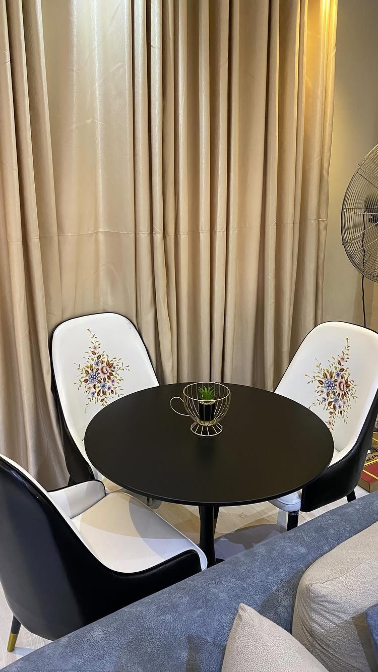 15 Apartment Decor Inspiration Ideas for Small Living Spaces 3 Small round black dining table with three floral patterned chairs against beige curtains.