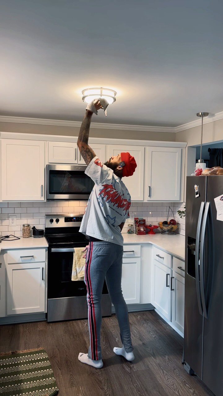 Apartment Deep Clean: 14 Areas to Scrub, Dust, and Vacuum 3 Person reaching up to clean a ceiling light fixture in a white kitchen.