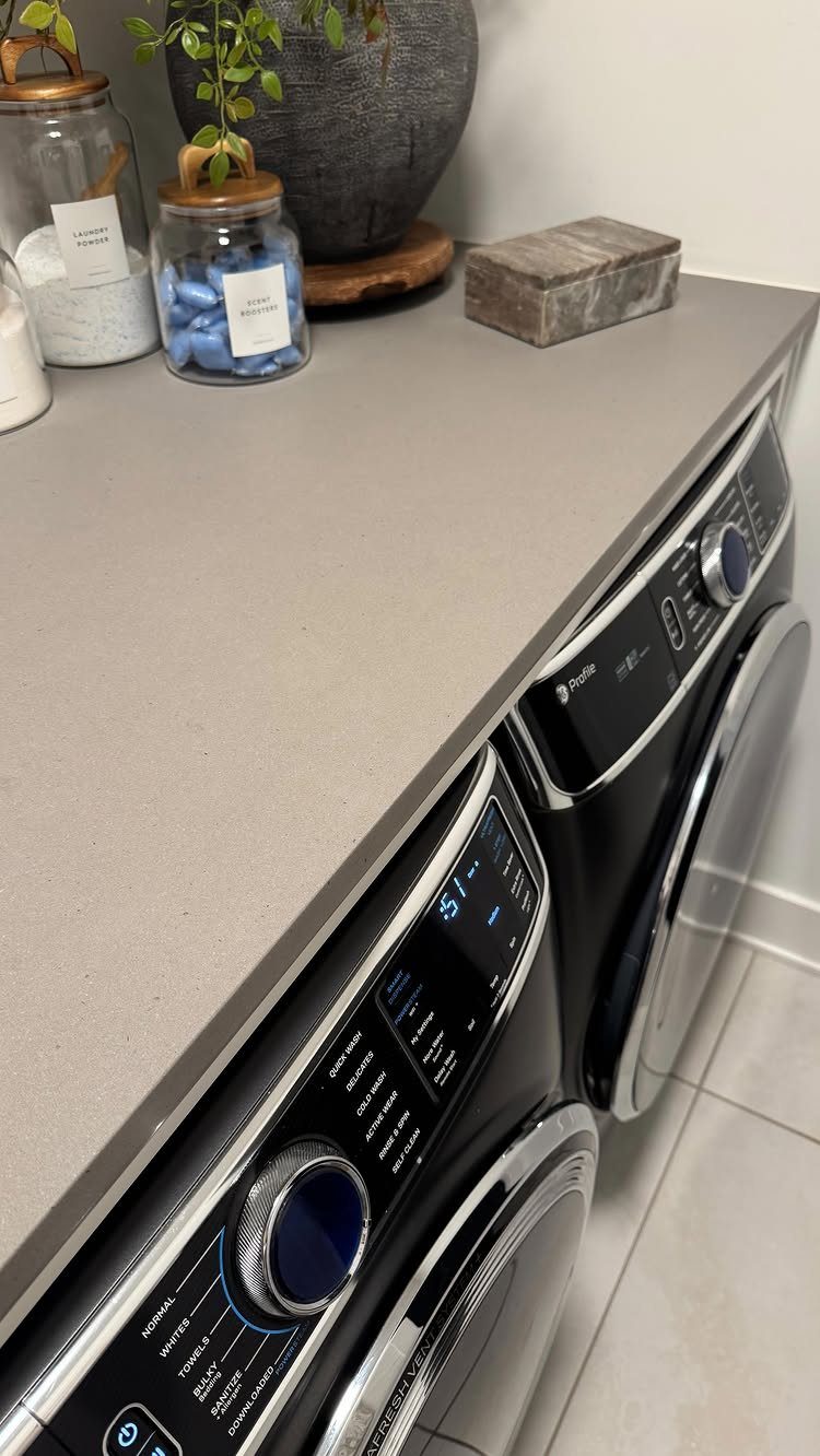 Apartment Deep Clean: 14 Areas to Scrub, Dust, and Vacuum 6 Clean black washer and dryer installed under a grey countertop in a laundry room.