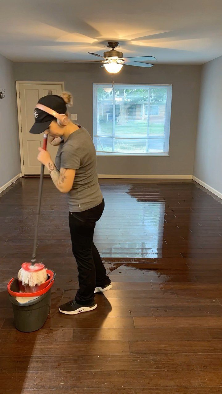 Apartment Deep Clean: 14 Areas to Scrub, Dust, and Vacuum 12 Person mopping dark hardwood floors in a bright room with grey walls.