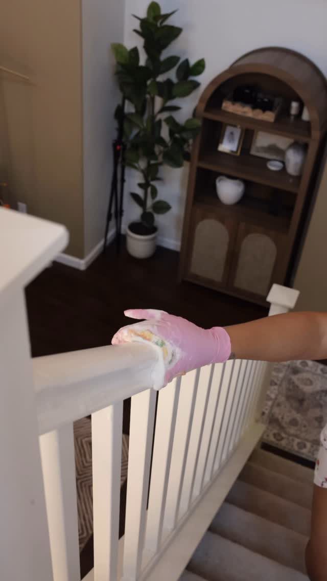Apartment Deep Clean: 14 Areas to Scrub, Dust, and Vacuum 5 Person in pink glove wiping a white wooden stair railing with a cloth.
