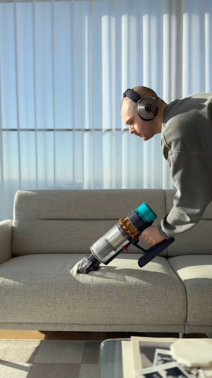 Apartment Deep Clean: 14 Areas to Scrub, Dust, and Vacuum 10 Man using a handheld vacuum to clean a light grey fabric sofa.