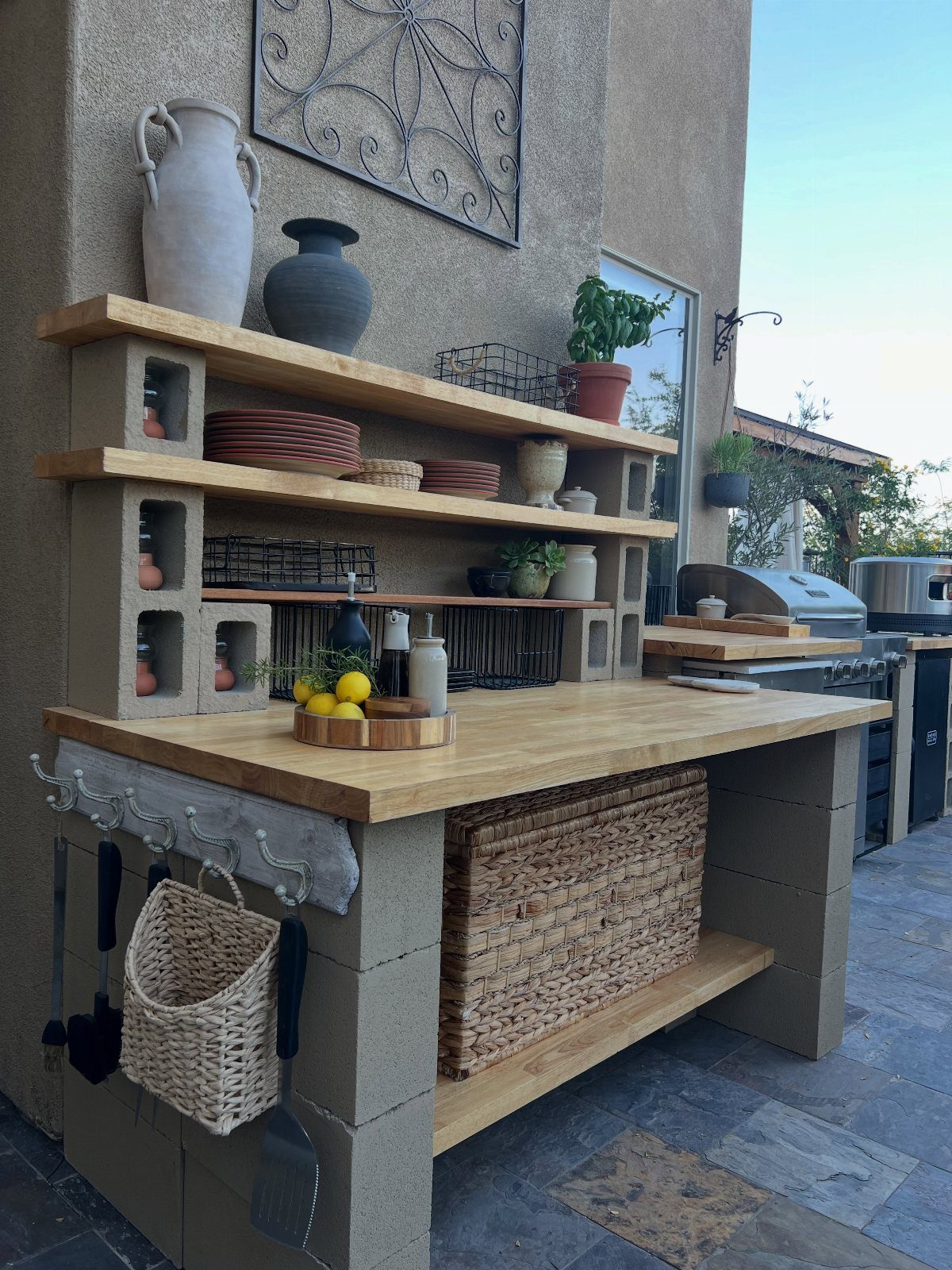 Cinder block outdoor kitchen island with wooden countertops and rustic shelving.