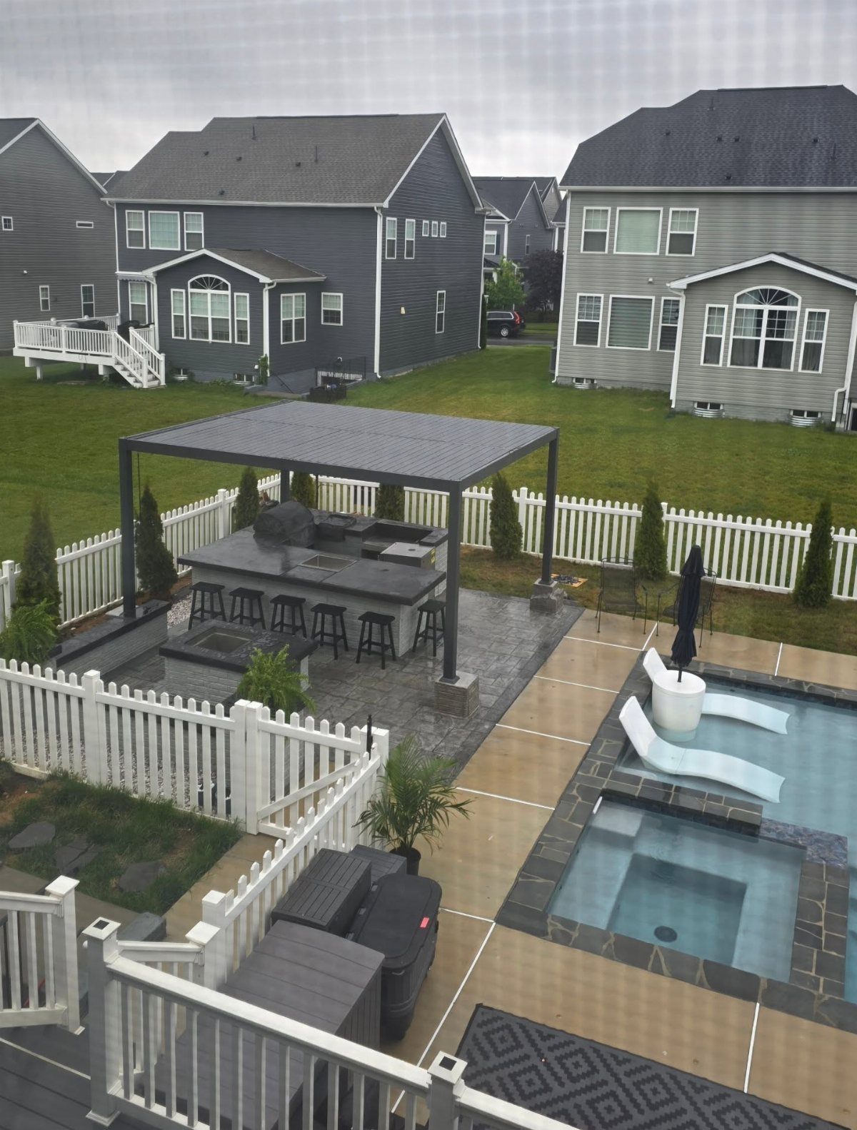 Outdoor kitchen island with seating under a pergola next to a swimming pool.