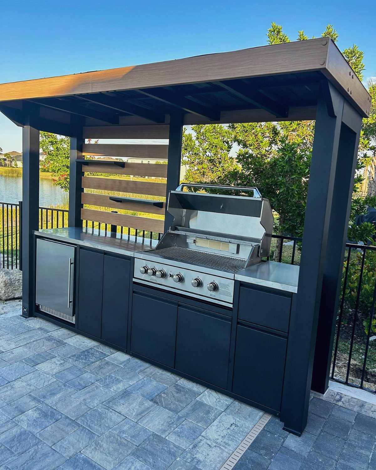 Modern black outdoor kitchen island with built-in grill under a dark pergola.