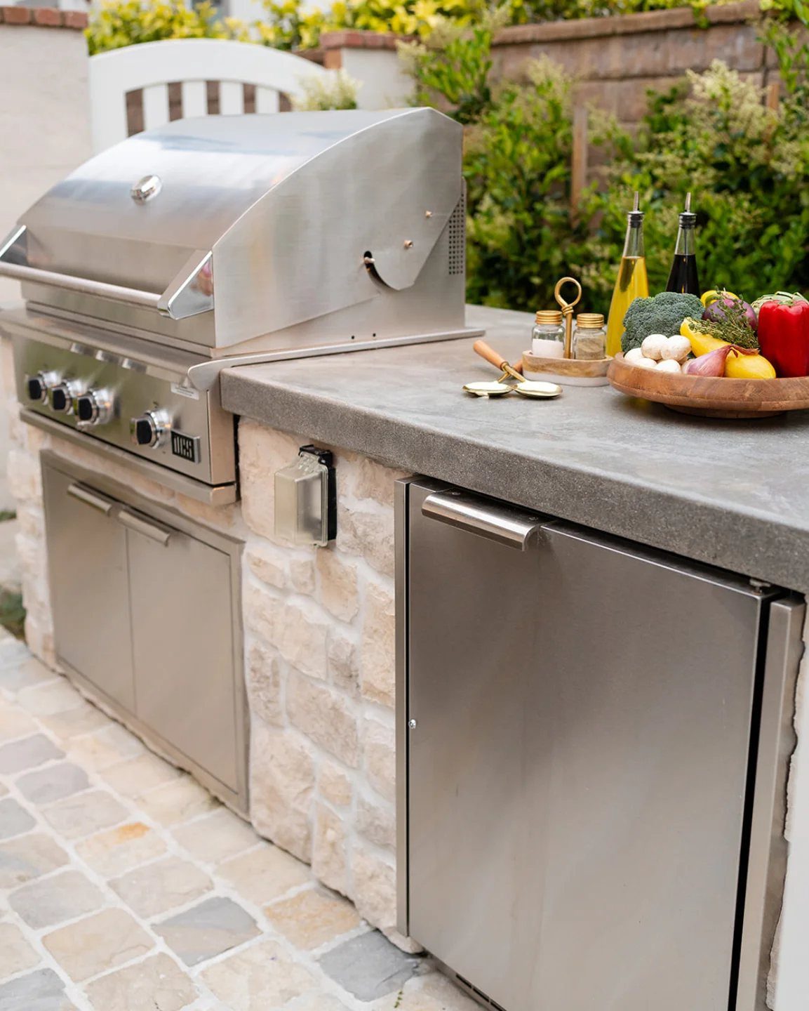 Outdoor kitchen island with light stone finish, concrete countertop, and stainless steel grill.