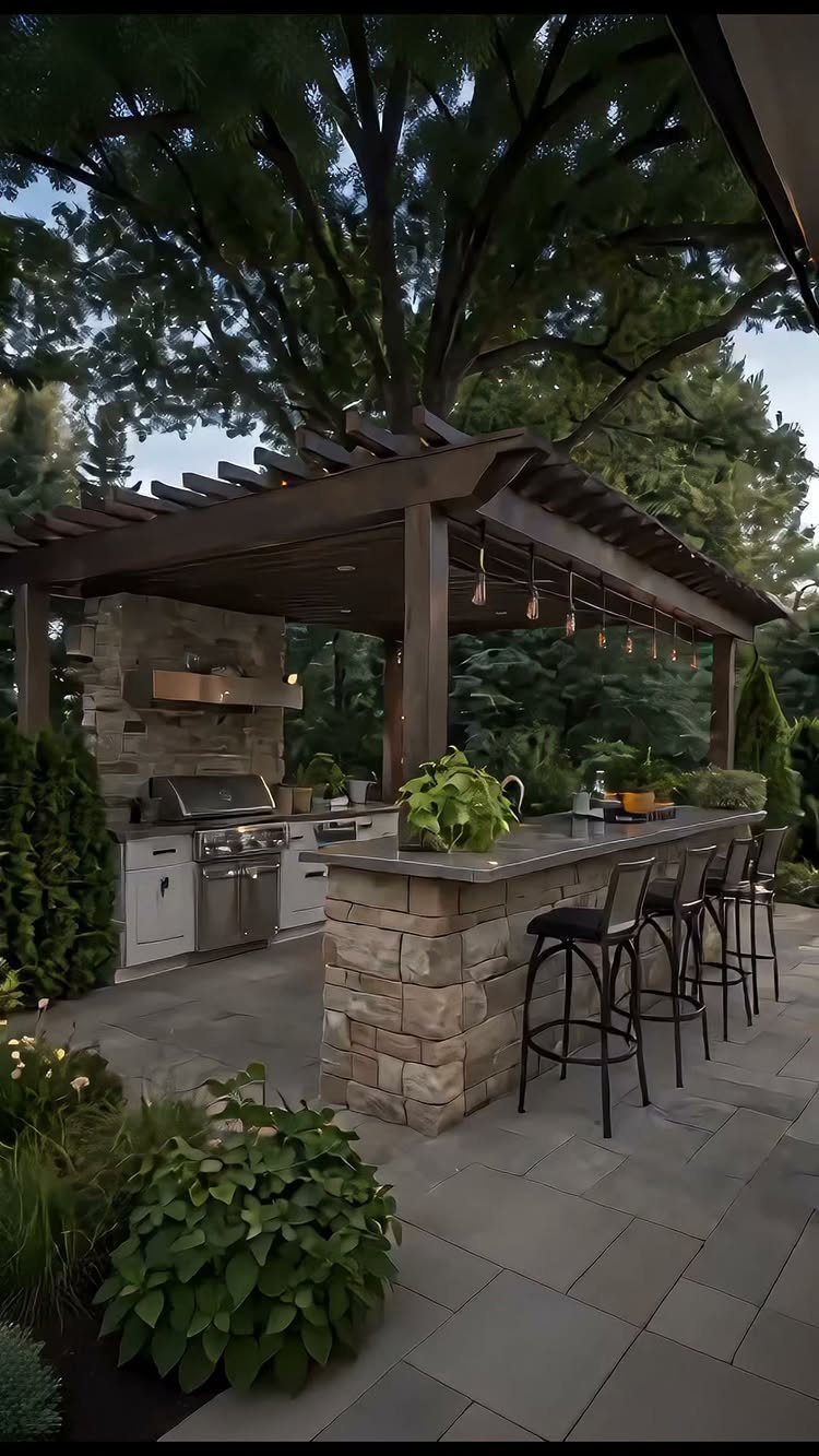 Stone outdoor kitchen with built-in grill and seating under a wooden pergola