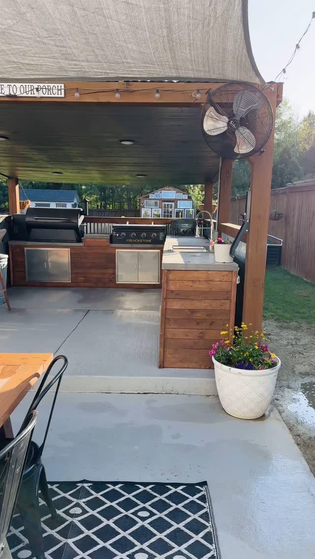 Outdoor kitchen island with wooden siding and built-in grill under a covered porch.