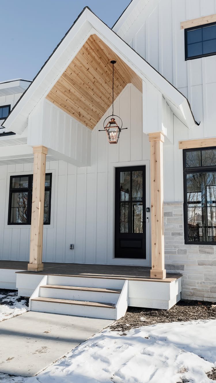 Board and Batten: 8 Styles That Update the Classic Wall Treatment 3 White farmhouse exterior with vertical board and batten siding and natural wood porch accents.