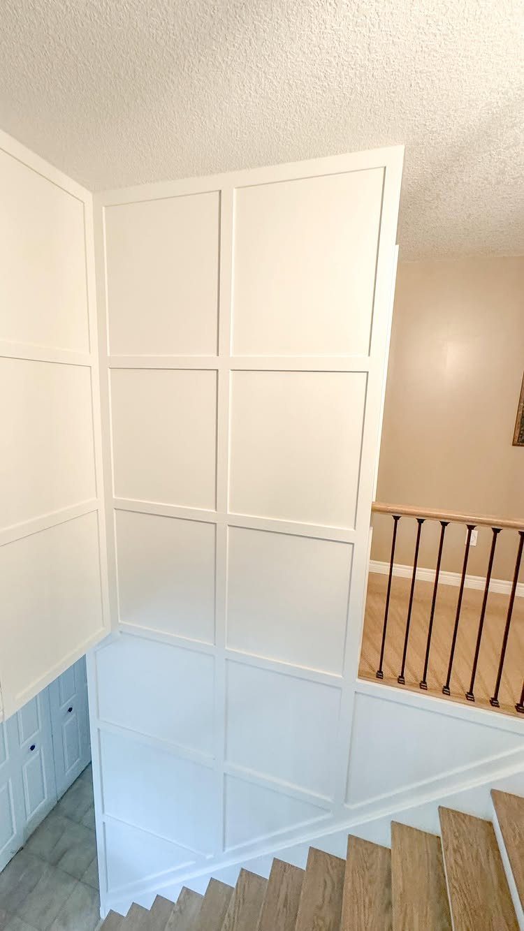 Board and Batten: 8 Styles That Update the Classic Wall Treatment 2 White square panel board and batten wall design next to a wooden staircase.