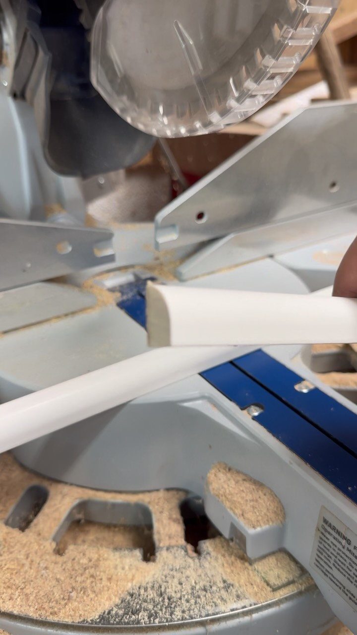 White moulding being prepared for cutting on a miter saw surrounded by sawdust.