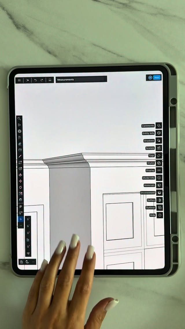 A hand using a digital tablet to view a detailed line drawing of wall moulding.