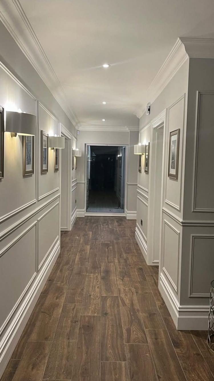 A long hallway featuring decorative white box moulding on light grey walls and wood flooring.