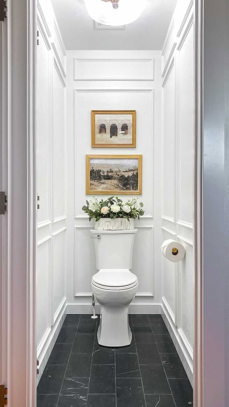 White box moulding panels on a bathroom wall behind a toilet and framed art.