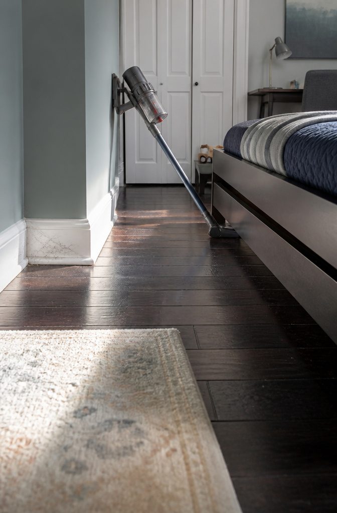Vacuum crevice tool cleaning the gap behind a bed along the baseboard