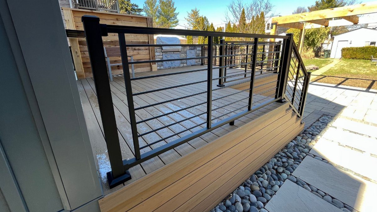 Modern wooden deck with black metal railings and grey river stone underpinning.