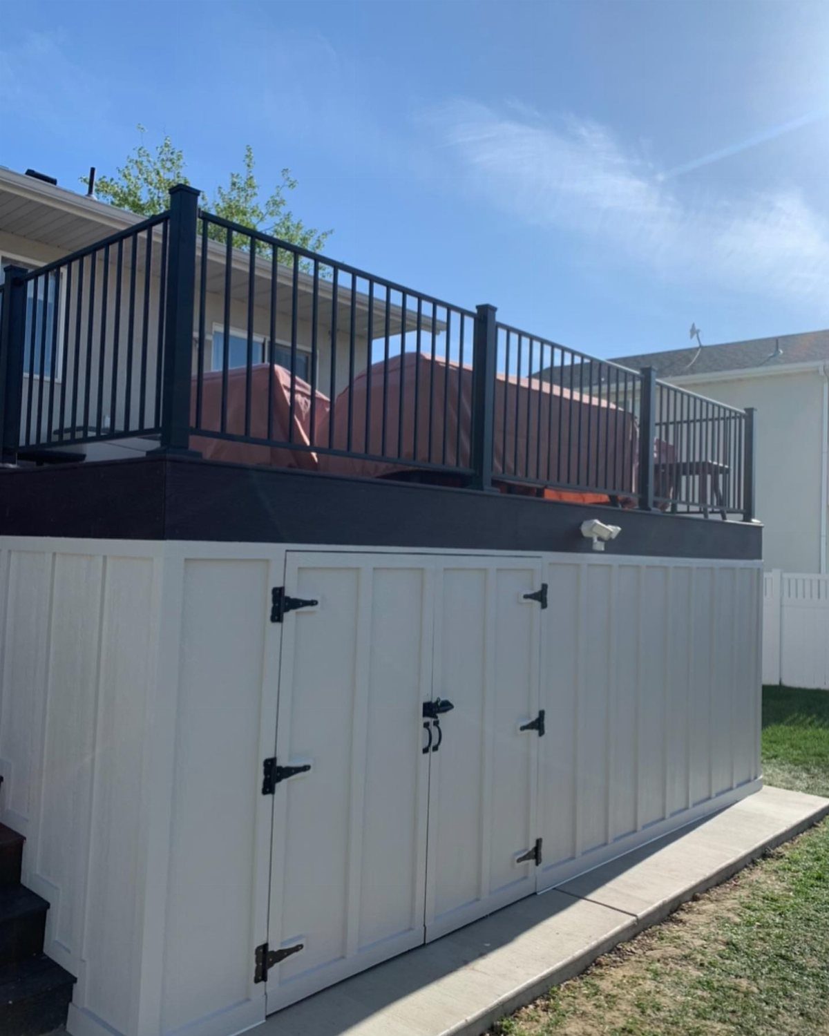 White enclosed storage shed built underneath a raised wooden deck with black railings.