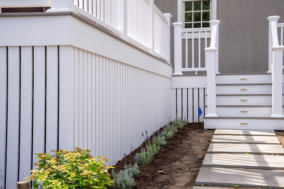 White raised deck with vertical white skirting boards and a stone paver walkway.