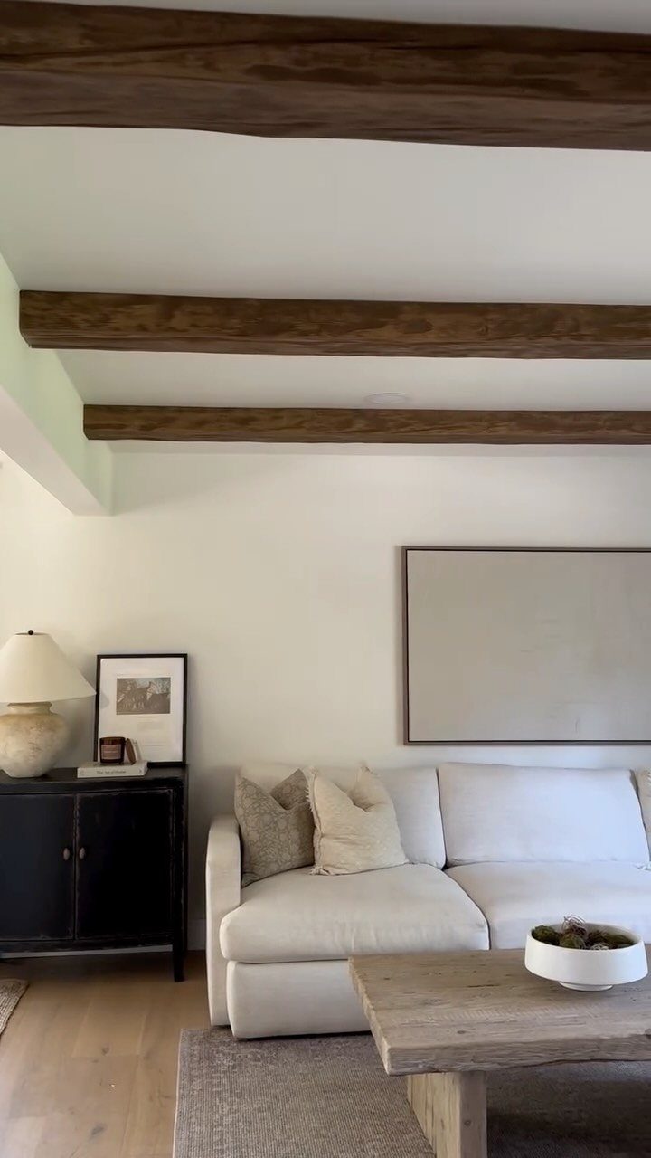 Wooden beams on a white ceiling above a modern white living room setup.