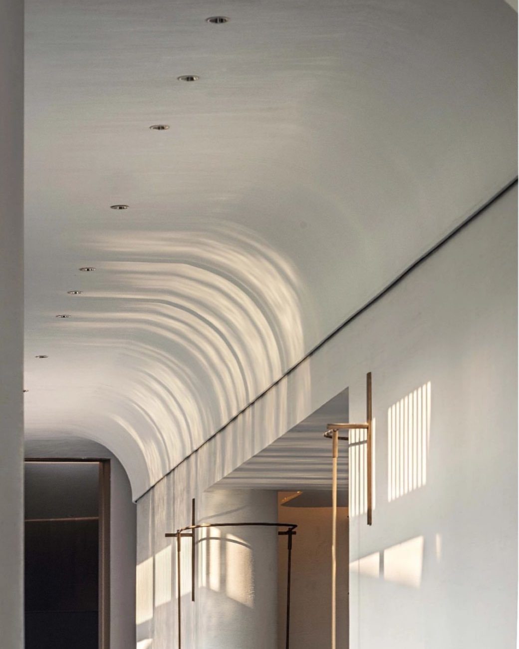 Curved white gypsum ceiling with wave-like ridges and recessed lighting in a modern hallway.
