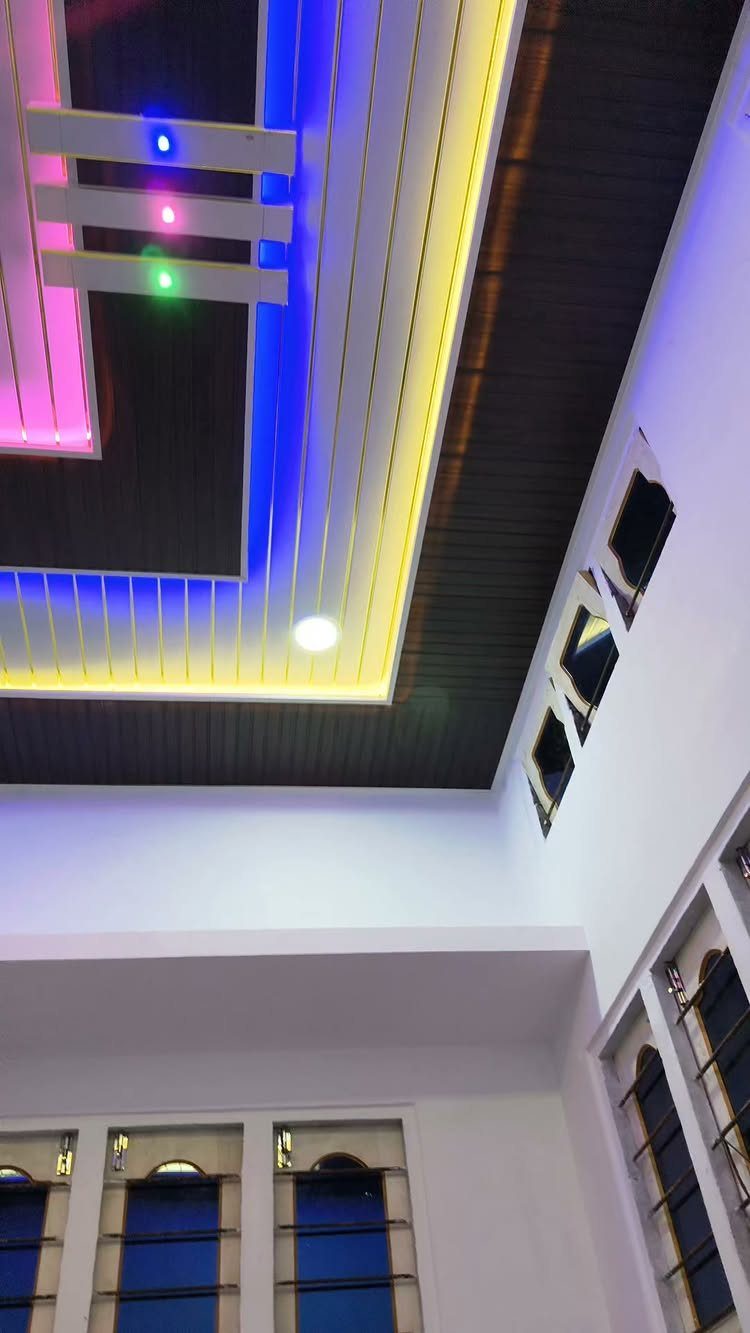 Modern living room ceiling with white and dark PVC panels and colorful LED lighting.