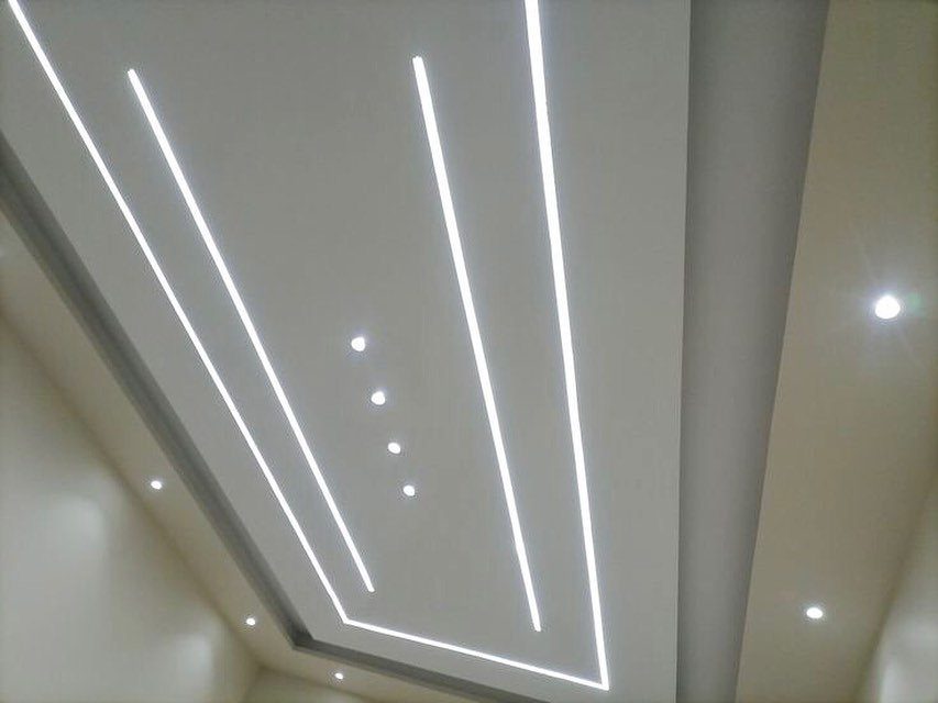 Modern white false ceiling with linear LED strips and recessed circular spotlights.