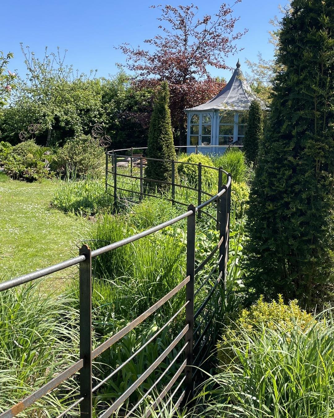 Fence Grill Design Modern: 28 Ideas from Steel to Aluminum 16 Black metal garden fence curving through a green landscape with a glass gazebo.