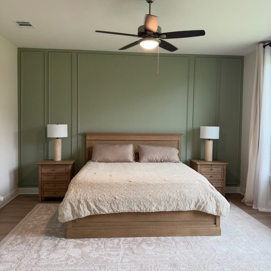 Sage green accent wall with large rectangular picture frame molding behind a wooden bed.