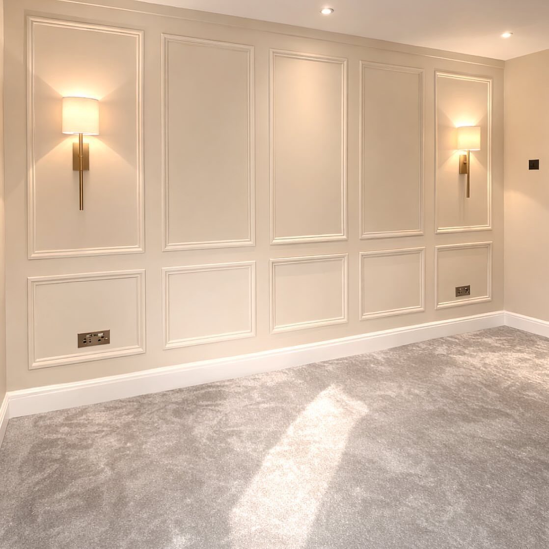 Beige wall with decorative French wall paneling and gold sconces in a carpeted room.
