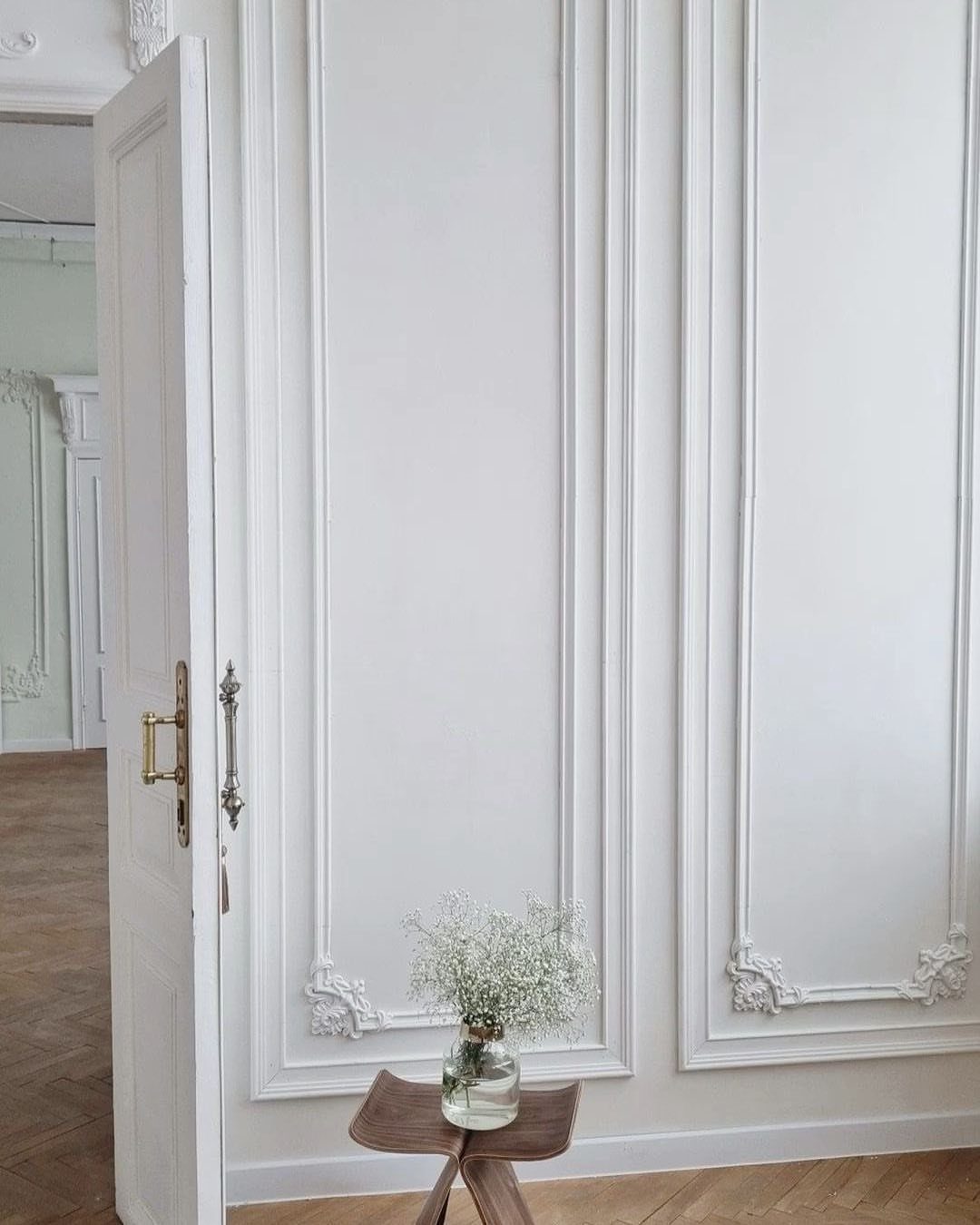 White decorative wall panels with ornate carvings and an open white door in a bright room.