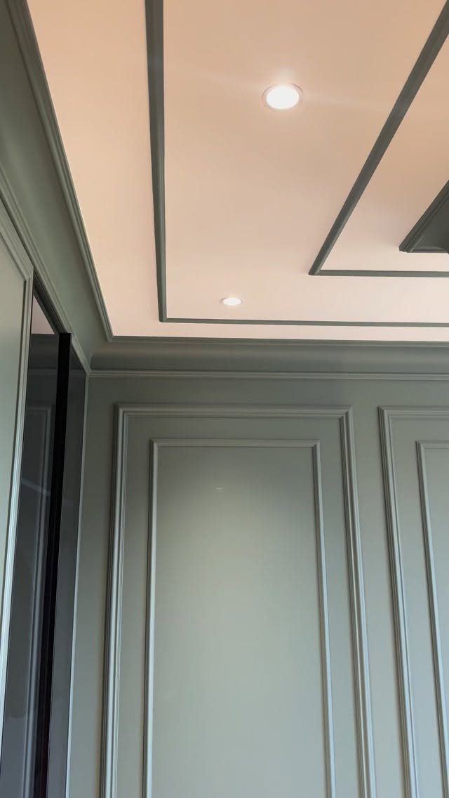 Sage green wall paneling with decorative moulding and a matching recessed ceiling design.