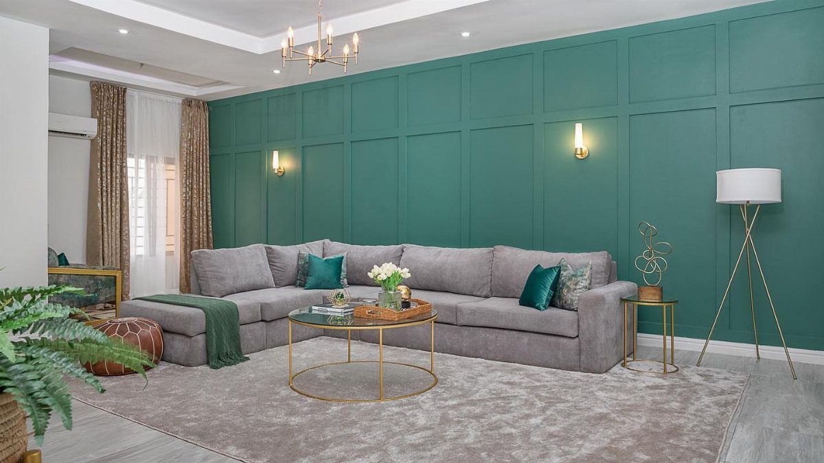 Teal wall with rectangular paneling behind a grey sectional sofa in a modern living room.