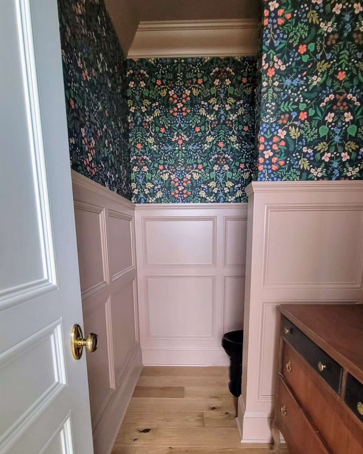 Pink wainscoting wall panels paired with dark floral patterned wallpaper in a small hallway.