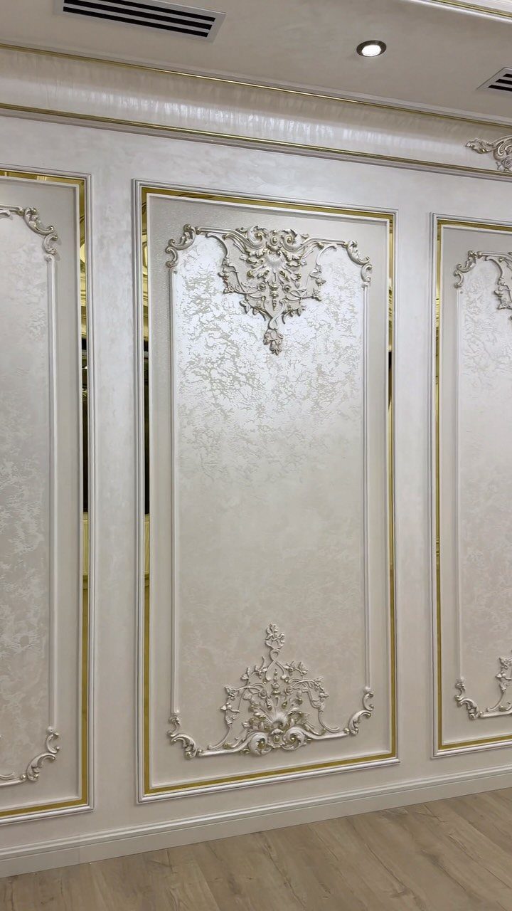 Ornate white wall panels with gold trim and decorative relief carvings on a light wall.