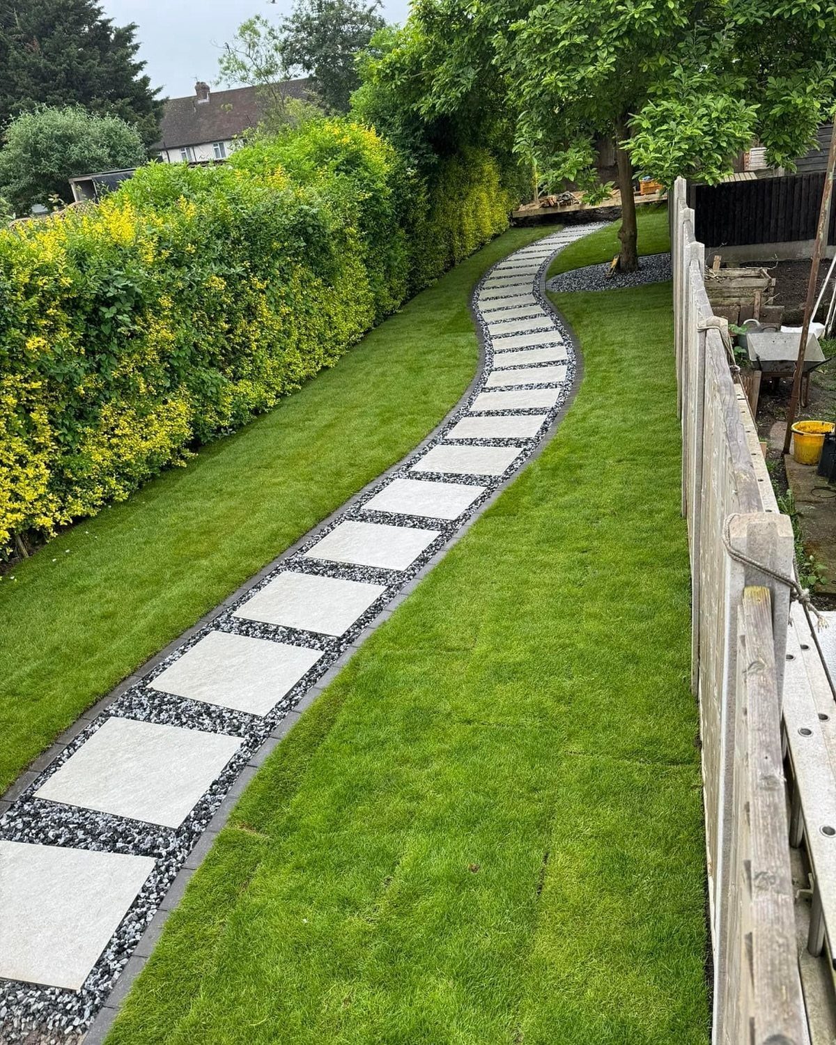20 Garden Ideas for Small Spaces, From Vertical to Fire Pits 18 Curved stone paver pathway winding through a green lawn with a yellow-green hedge.