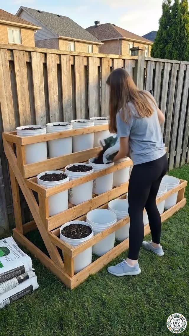 20 Garden Ideas for Small Spaces, From Vertical to Fire Pits 6 Woman planting greenery in white buckets held by a tiered wooden garden frame.