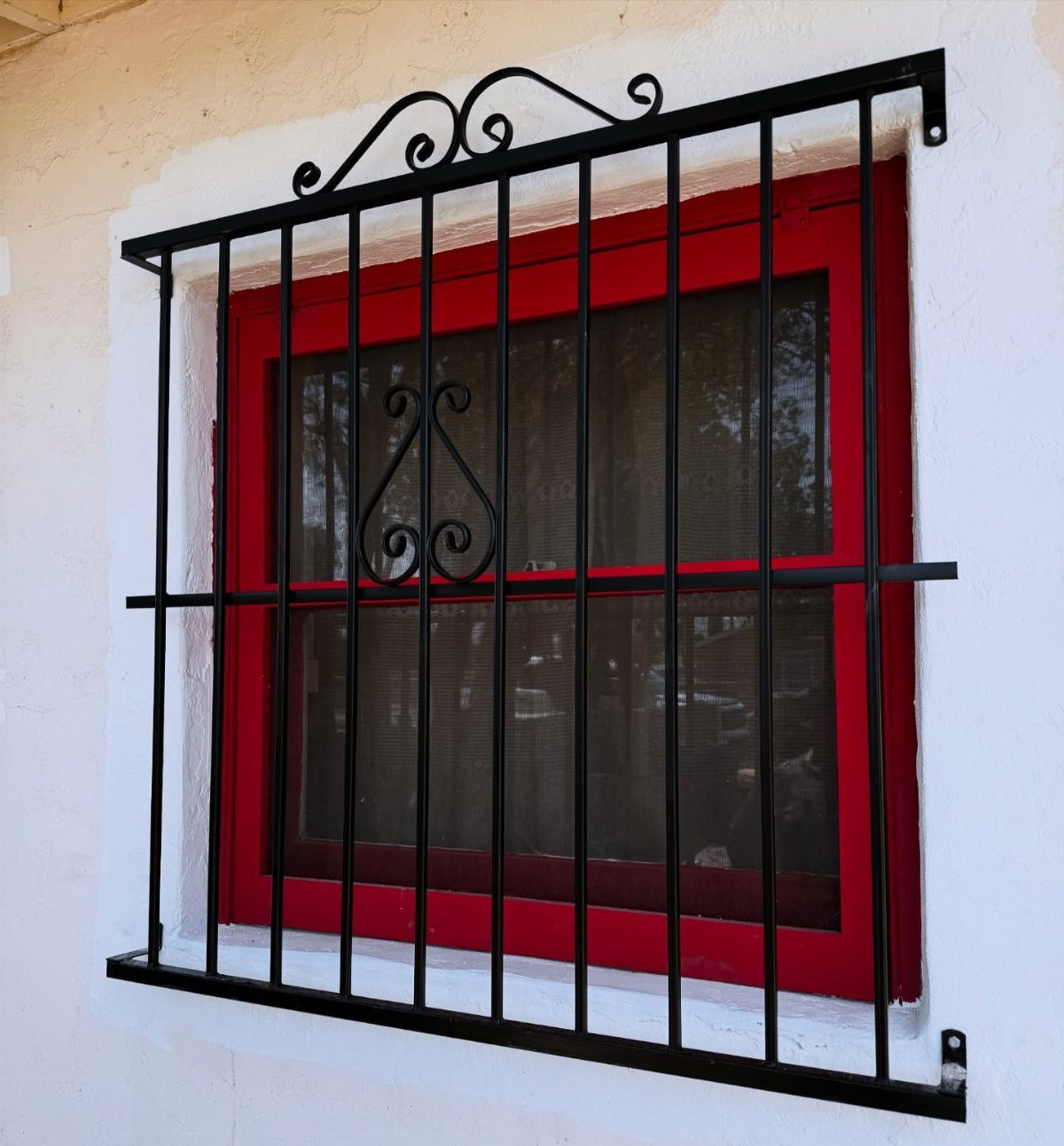 Black wrought iron window grill with decorative scrolls over a red window frame.