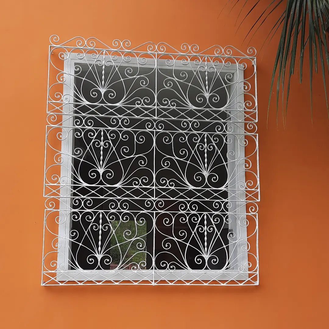 White decorative wrought iron window grille on a bright orange exterior wall