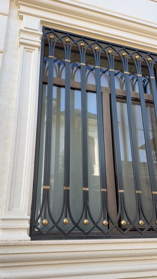 Black metal window grill with pointed Gothic arches and gold circular accents.