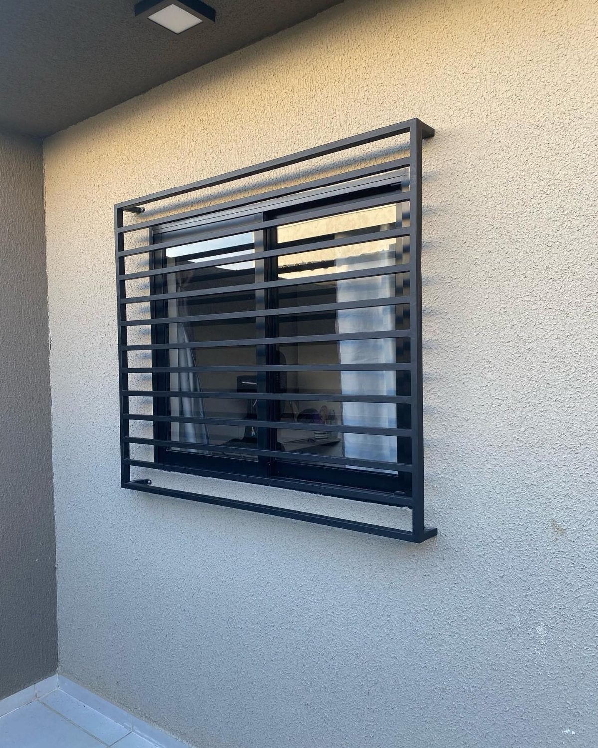 Black horizontal bar window grill installed on a beige textured exterior wall.