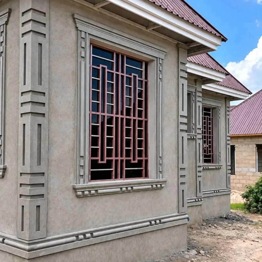 Reddish-brown geometric metal window grills on a grey concrete house exterior.