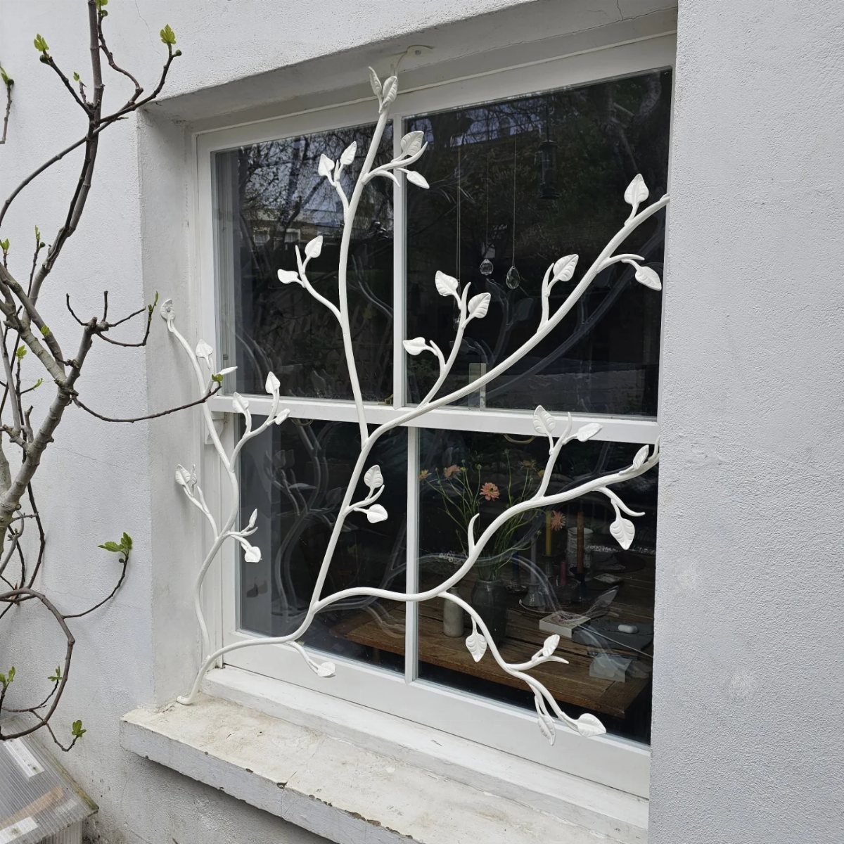White metal window grill with organic leaf and branch patterns on a window.
