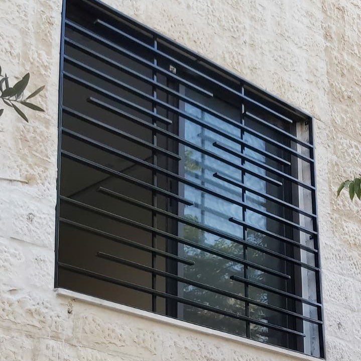 Black metal window grill with slim horizontal bars on a stone wall.