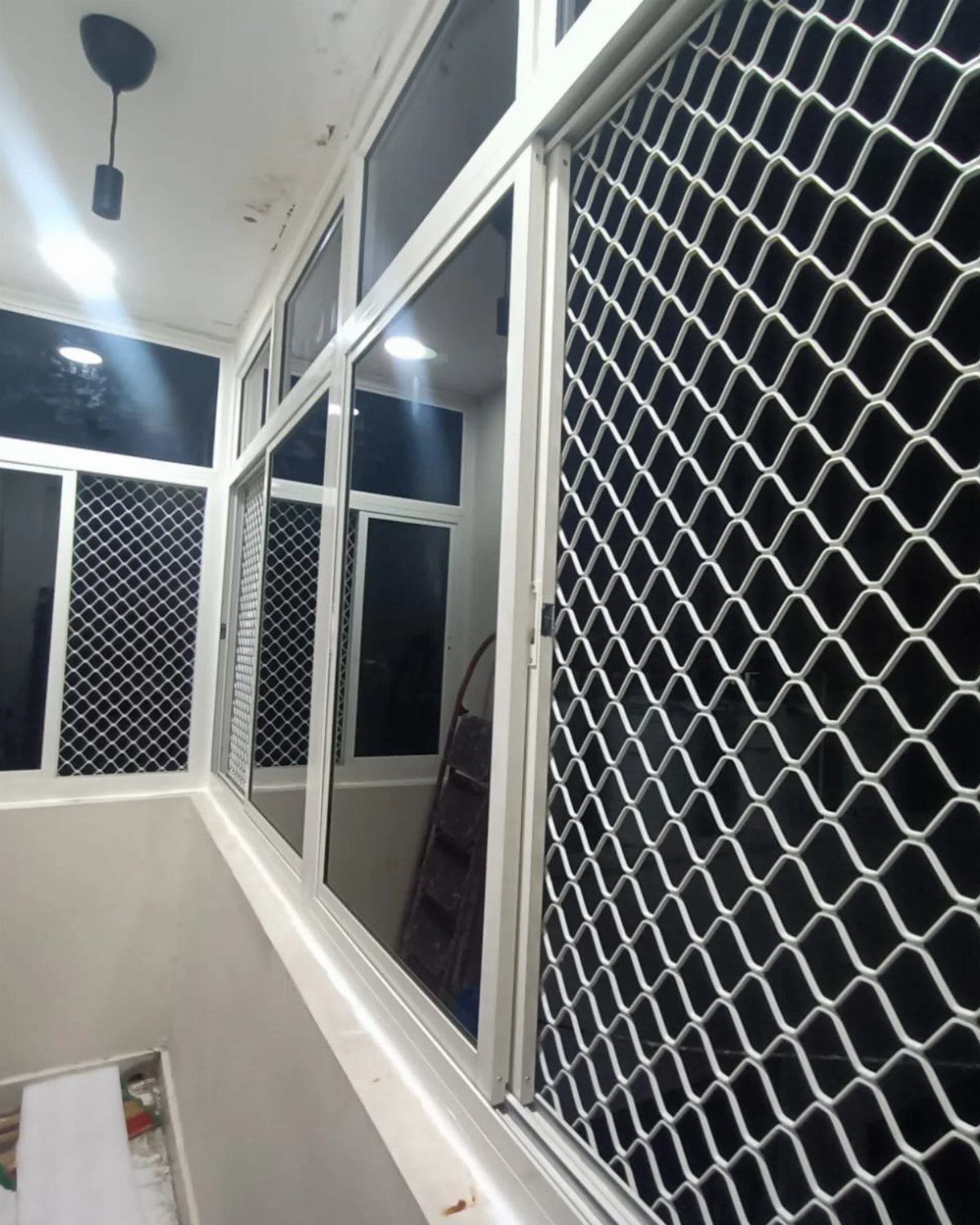 White window frames with sliding glass and diamond-patterned security grill mesh.