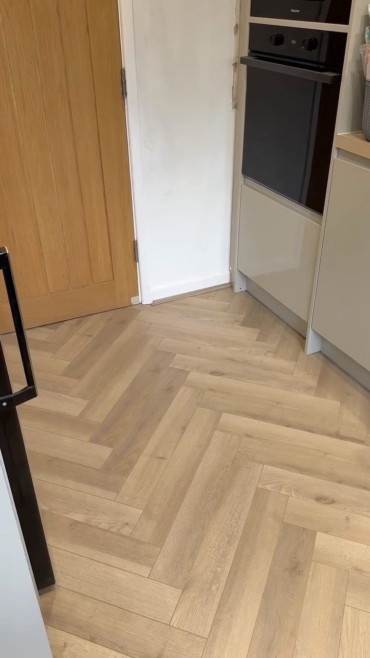Honey Oak Wood Floors: 8 Design Ideas That Work 4 Light wood herringbone pattern flooring in a kitchen with white cabinets and a wooden door.