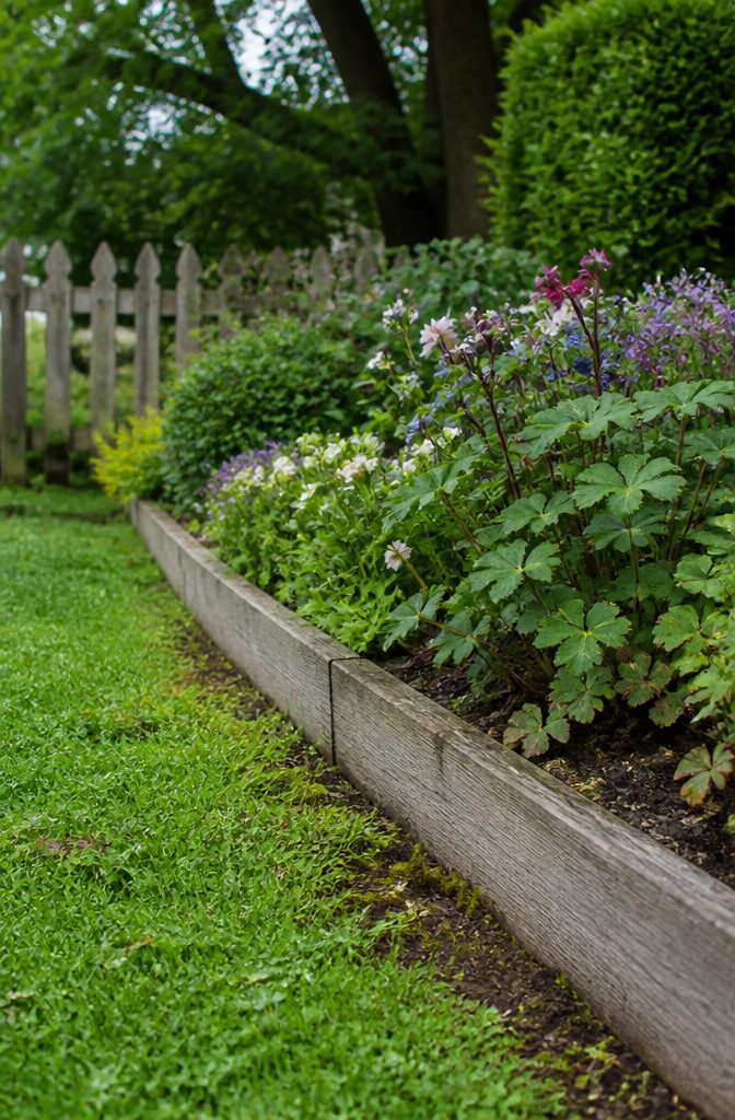 Landscape Bed Edging: Materials, Styles and How They Hold Up 6 Pale weathered wood boards edging a flower bed beside a narrow lawn strip