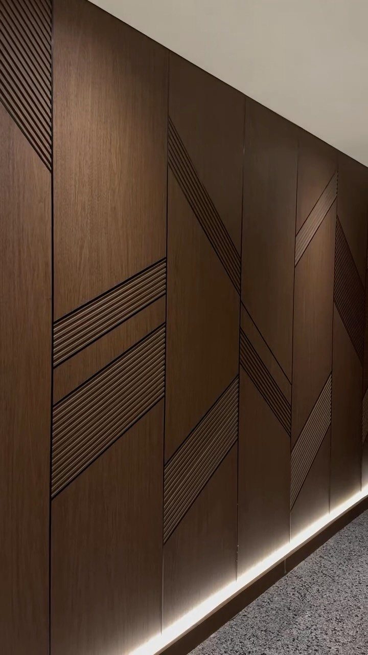 Dark wood wall paneling with geometric textured inlay patterns and floor lighting.