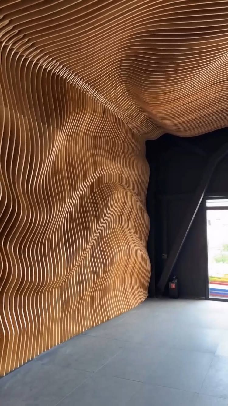 Wavy wooden slat installation forming an organic, sculptural wall and ceiling in a dark room.