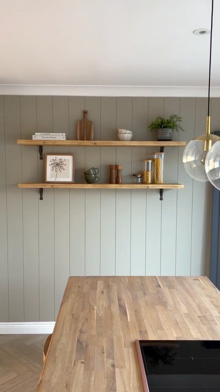 Sage green tongue-and-groove wall paneling with wooden floating shelves and kitchen decor.